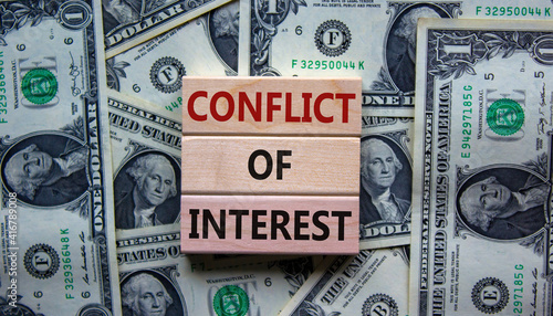 Conflict of interest symbol. Wooden blocks with words 'conflict of interest'. Beautiful background from dollar bills. Copy space. Business and conflict of interest concept.