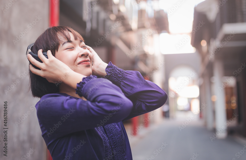 Happy young asian woman listening to music with headphones on the street.