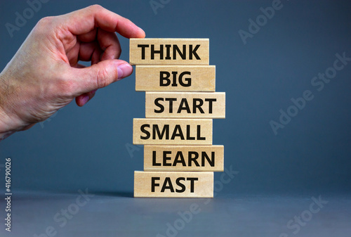 Think big start small symbol. Words 'Think big start small learn fast' on wooden blocks on a beautiful grey background. Businessman hand. Business, motivational and think big start small concept.