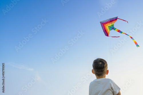Little boy in white shirt, playing with Colorful kite in the blue sky, with copy space.