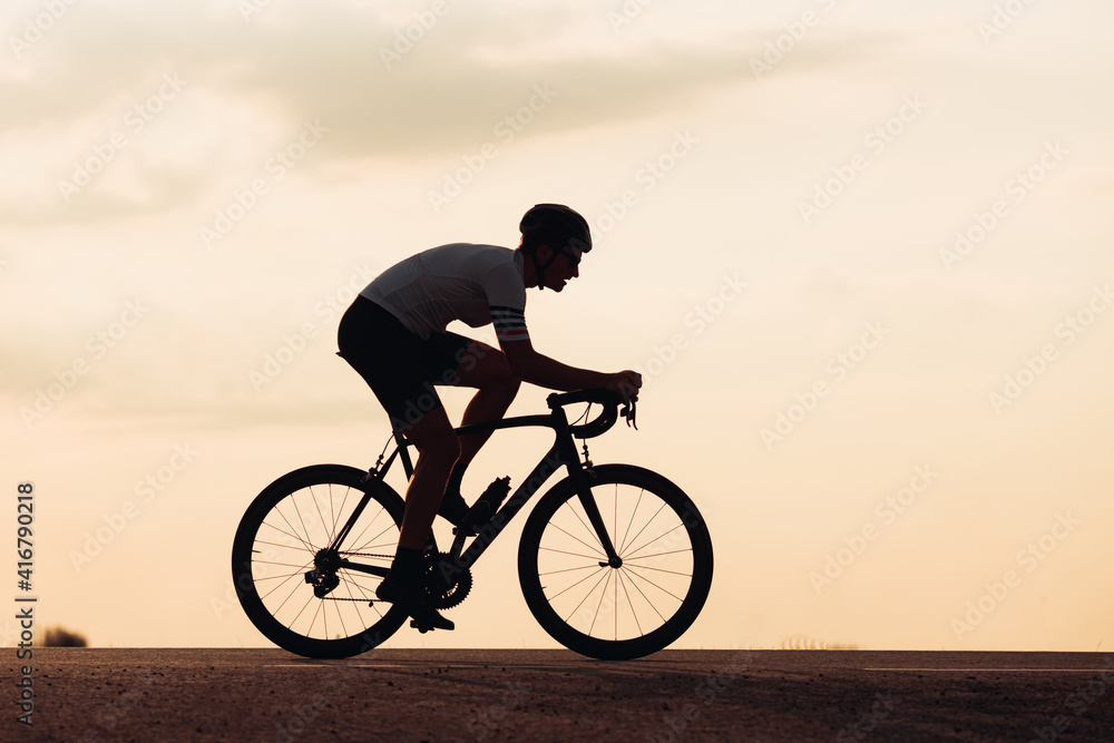 Fototapeta premium Silhouette of man in helmet riding bike during sunset