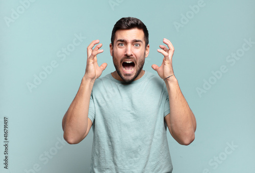 young handsome adult man screaming with hands up in the air, feeling furious, frustrated, stressed and upset