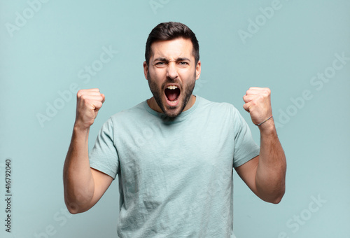young handsome adult man shouting aggressively with an angry expression or with fists clenched celebrating success