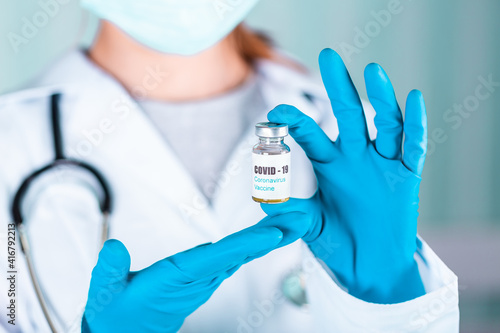 Doctor or nurse in uniform and gloves wearing face mask protective in lab holding medicine vial vaccine bottle with COVID-19 Coronovirus vaccine label