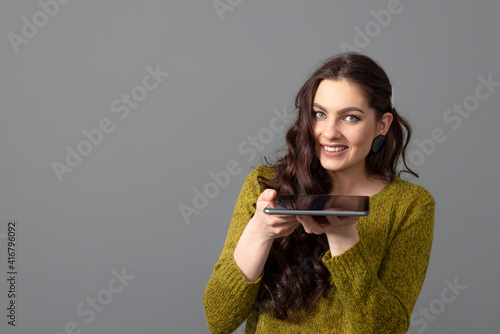 teenage female with long wavy hair having fun with a tablet, isolated on a gray background