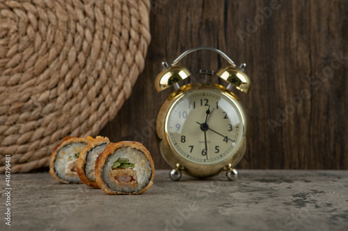 Set of breaded sushi hot rolls with an alarm clock on stone table