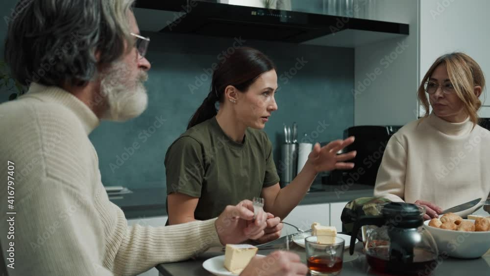 A beautiful young woman wearing military uniform is talking while having dinner with her family sitting inside the house A beautiful young woman wearing military uniform is talking while having dinner with her family sitting inside the house