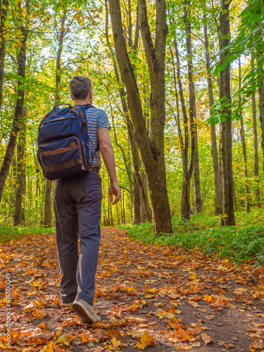 A middle-aged man with a backpack is walking in the woods.