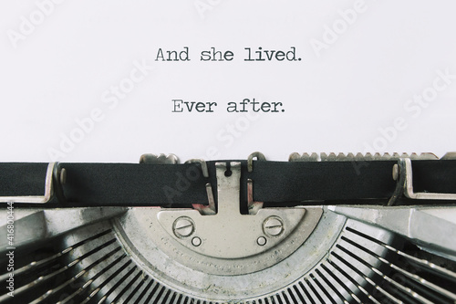 The ending phrase And she lived, ever after, printed on a paper page inside an old vintage typewriter. Closeup shot.
