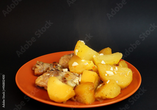 stewed potatoes with chicken and garlic in a ceramic plate on a black background