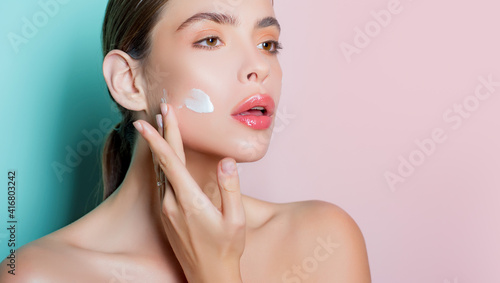 Closeup portrait of girl with healthy clean skin. Attractive young woman putting anti-aging cream on her face.
