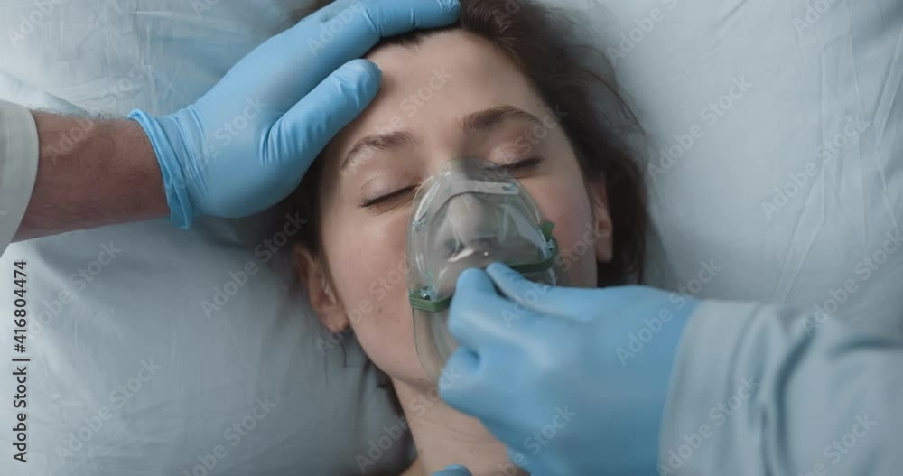Close up of doctor in protective gloves putting oxygen mask on sick young woman