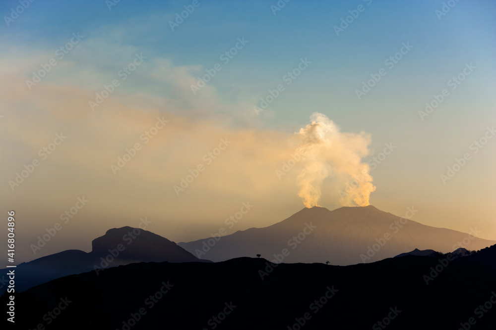 View of the silhouette of the Etna volcano erupting from the Peloritani mountains in Sicily Italy