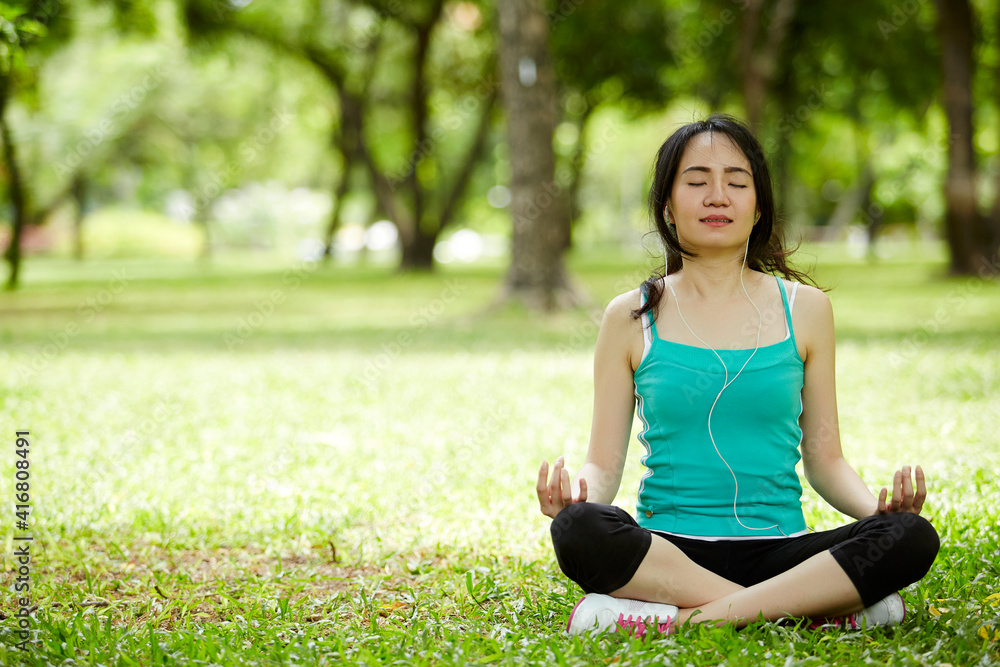 A beautiful woman with earbuds doing yoga meditation outdoor in a park A beautiful woman with earbuds doing yoga meditation outdoor in a park