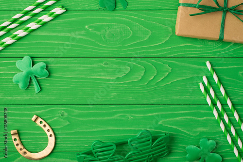 Happy St. Patrick's day concept. Flat lay top above overhead close up view photo image of present box drink straw gold horseshoe disco eyeglasses and clover leaves isolated bright color green backdrop