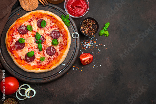 Fresh, delicious pizza and ingredients on a brown background. Top view with copy space.
