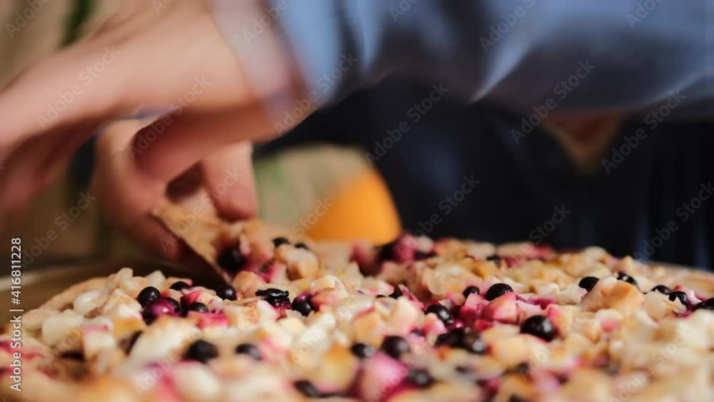 The guy takes a slice of sweet pizza. Large round sweet pizza pie with apple pieces, berries, almond slices and condensed milk. Close-up. The guy takes a slice of sweet pizza. Large round sweet pizza pie with apple pieces, berries, almond slices and condensed milk. Close-up.