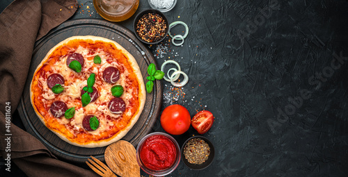 Culinary panorama with pizza with salami and cheese and ingredients on a black background.