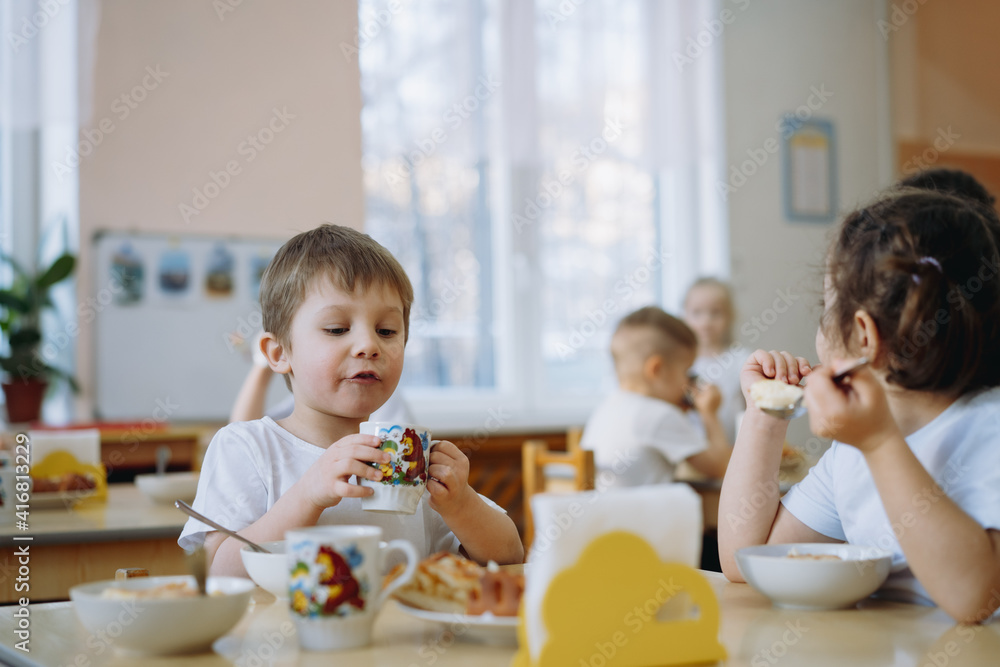 cute little boy eating cakes
and drinking tea having breakfast in kindergarten. Image with selective focus cute little boy eating cakes
and drinking tea having breakfast in kindergarten. Image with selective focus
