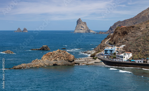 The northeast side of the Atlantic island of Tenerife with the impressive rocks in the sea. On the right are some buildings with restaurants. The most famous rock can be seen in the background.