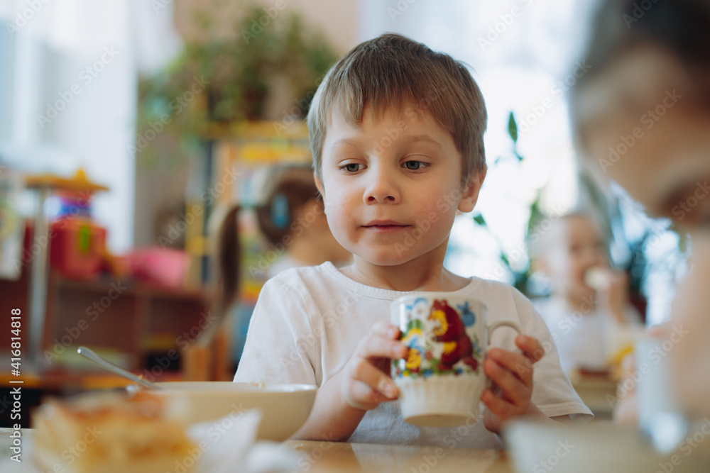 cute little boy eating cake and drinking tea having breakfast in kindergarten. Image with selective focus cute little boy eating cake and drinking tea having breakfast in kindergarten. Image with selective focus