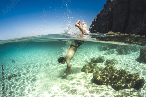 Young man swimming in crystal clear waters of the Mediterranean Sea with underwater camera