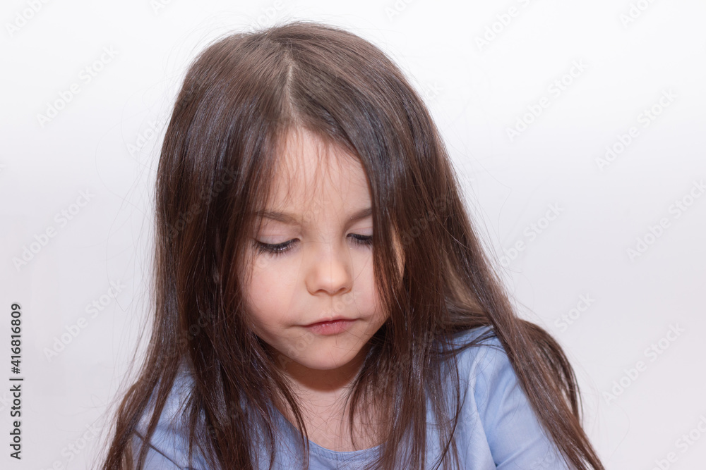 Sad little child sits on the floor in the studio on a white background. Beautiful cute preschooler girl with long straight hair Sad little child sits on the floor in the studio on a white background. Beautiful cute preschooler girl with long straight hair