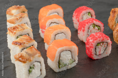 Set of delicious fresh sushi rolls on black surface