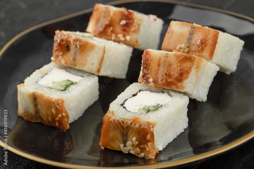 Black plate of dragon sushi rolls with eel on black surface Black plate of dragon sushi rolls with eel on black surface