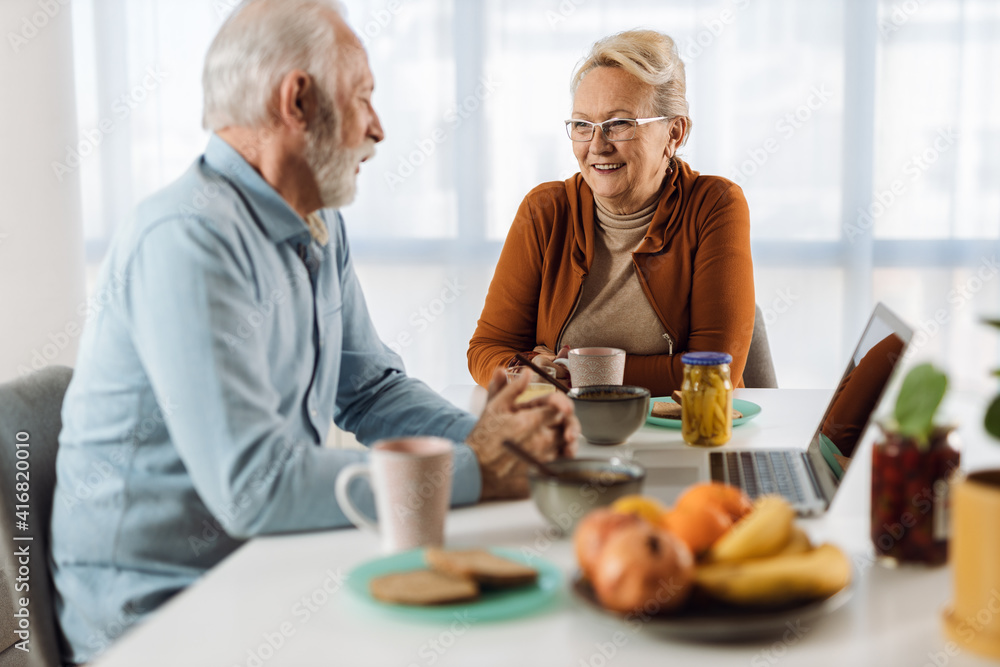 Happy mature couple communicating while having breakfast at dining table Happy mature couple communicating while having breakfast at dining table