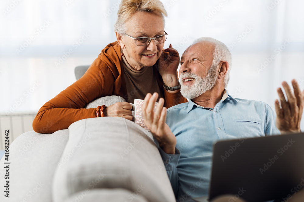 Obraz premium Cheerful senior couple relaxing on sofa in the living room and using laptop