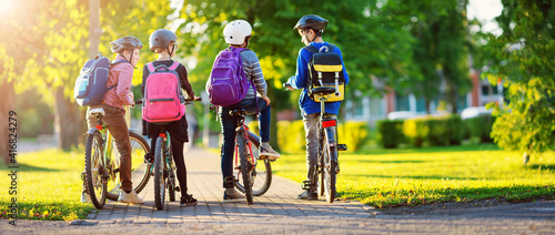 Foto Children with rucksacks riding on bikes in the park near school