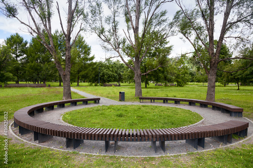 Round wooden bench in the park, standing under the trees. Modern fashionable design round circular bench in the garden.