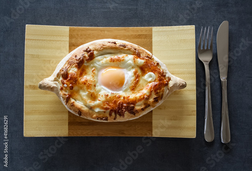 Georgian baked bread stuffed with cheese , on the wooden plate with black background photo