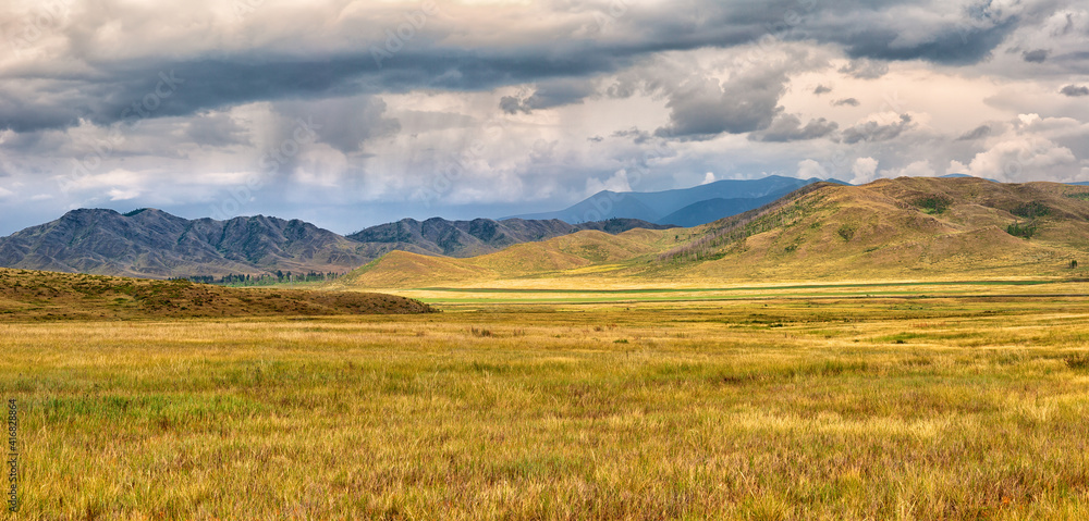 Amazing landscape of yellow steppe and mountains. Storm clouds and rain in the mountains.