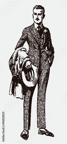Stylish young man from early 20th century wearing three piece check plaid tweed suit and holding hat and overcoat