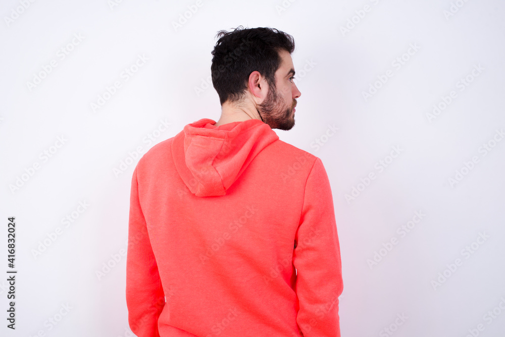 The back view of young Caucasian bearded man wearing pink hoodie against white wall Studio Shoot. The back view of young Caucasian bearded man wearing pink hoodie against white wall Studio Shoot.