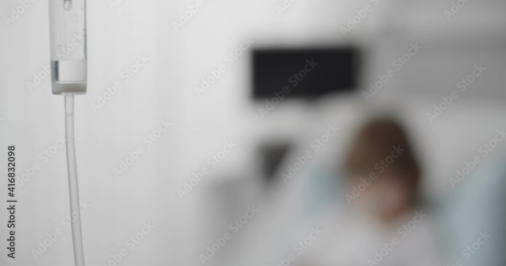Preteen kid patient lying in hospital bed using tablet with dropper in hand Preteen kid patient lying in hospital bed using tablet with dropper in hand