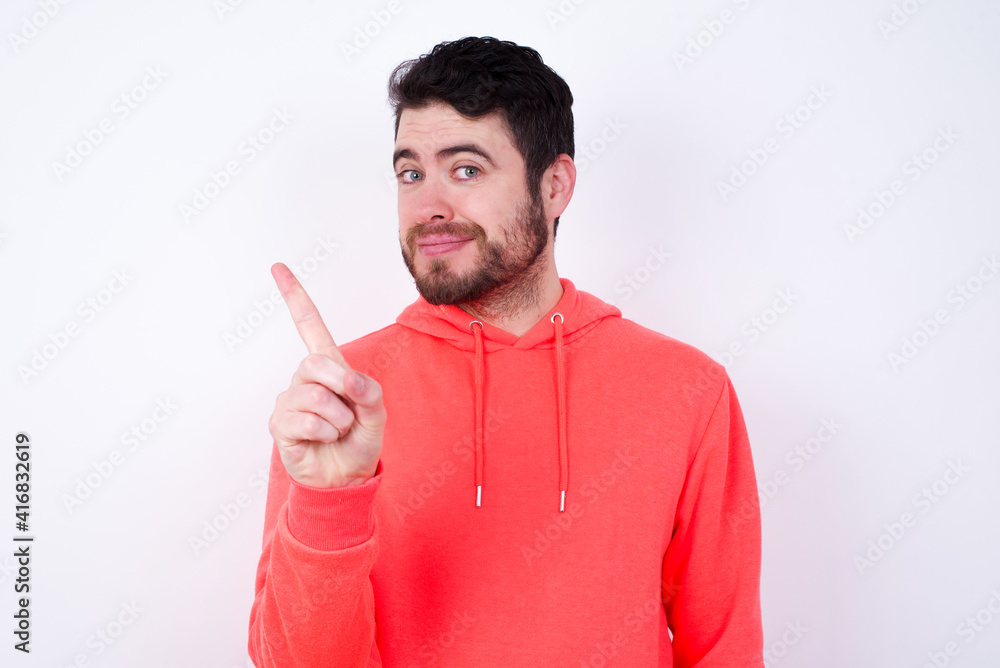 No sign gesture. Closeup portrait unhappy young Caucasian bearded man wearing pink hoodie against white wall raising fore finger up saying no. Negative emotions facial expressions, feelings. No sign gesture. Closeup portrait unhappy young Caucasian bearded man wearing pink hoodie against white wall raising fore finger up saying no. Negative emotions facial expressions, feelings.