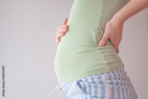 Pregnant woman holding hands on her belly. Belly of a pregnant woman on 16 week, 4 month. A woman is stroking her belly in the second trimet of pregnancy
