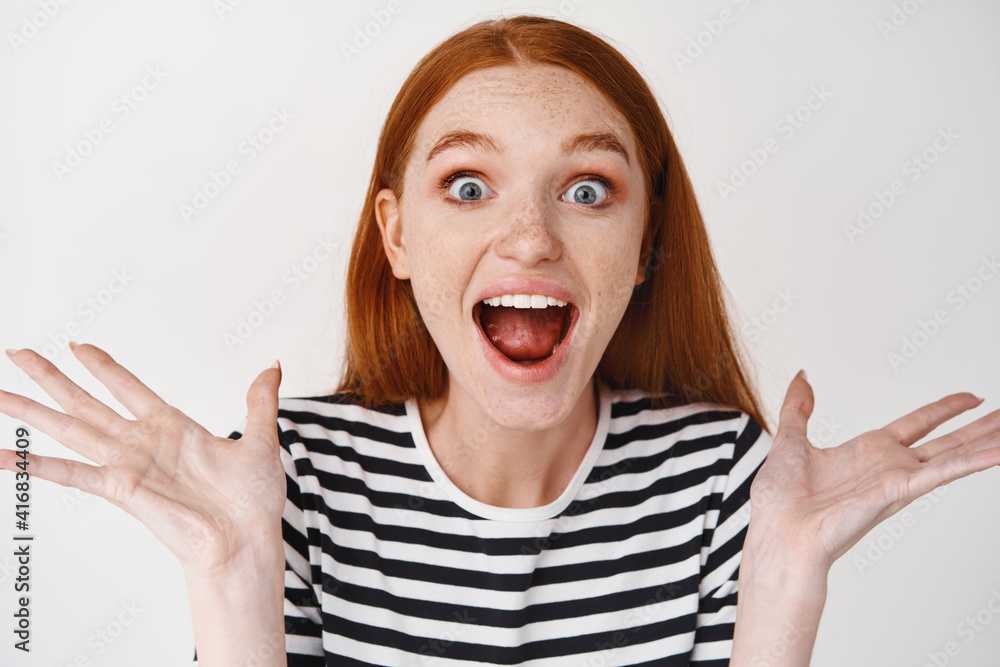 Close-up of happy redhead woman shouting from joy and happiness, looking surprised, standing over white background Close-up of happy redhead woman shouting from joy and happiness, looking surprised, standing over white background