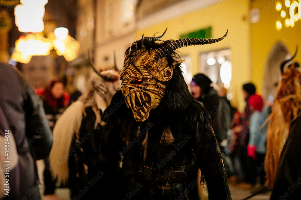 Fototapeta premium Krampus night parade, People in scary fur costumes and masks with hornes walk on the street, Traditional show before Christmas, historical street Getreidegasse, Salzburg, Austria