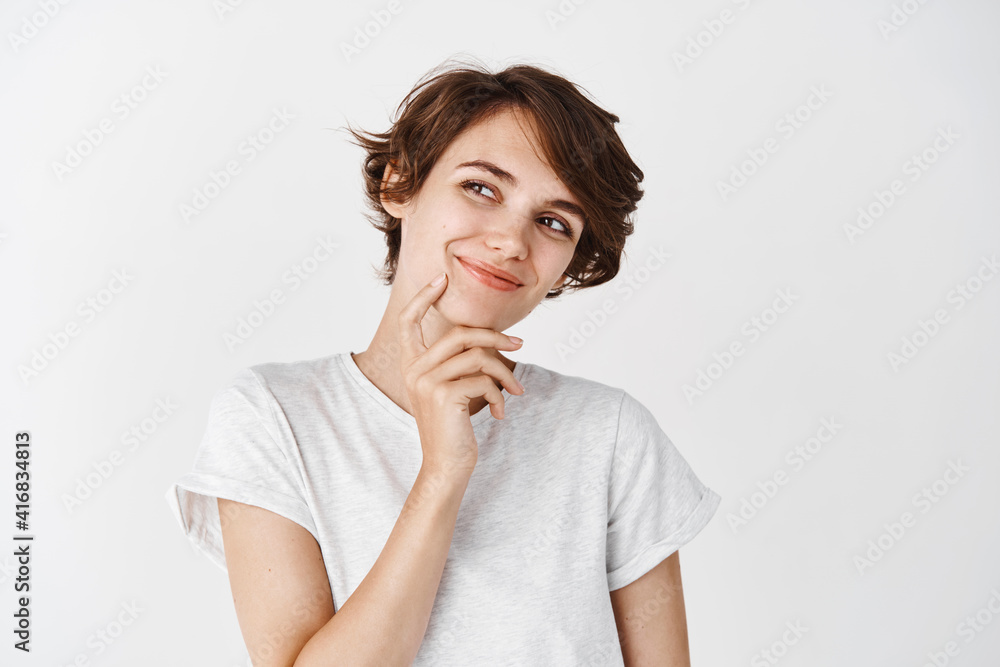 Portrait of natural young woman with short hairstyle, looking pensive aside, smiling and dreaming of something, standing thoughtful on white background Portrait of natural young woman with short hairstyle, looking pensive aside, smiling and dreaming of something, standing thoughtful on white background