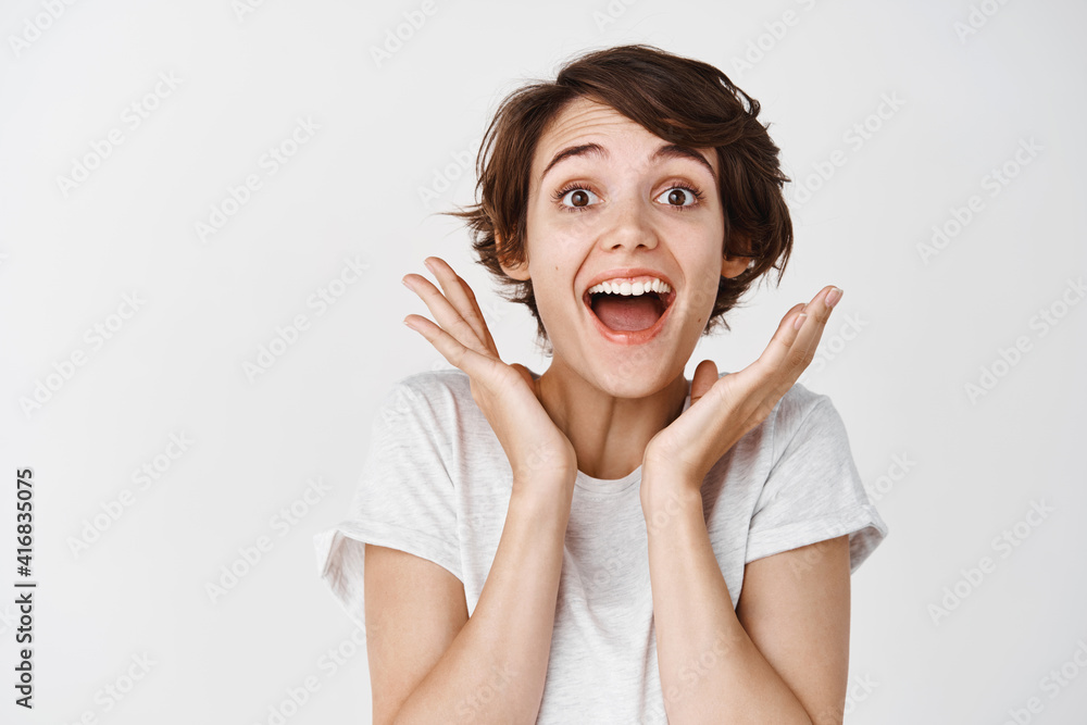 Close-up of surprised and happy woman gasping amazed, saying wow astounded, look fascinated at camera, white background Close-up of surprised and happy woman gasping amazed, saying wow astounded, look fascinated at camera, white background