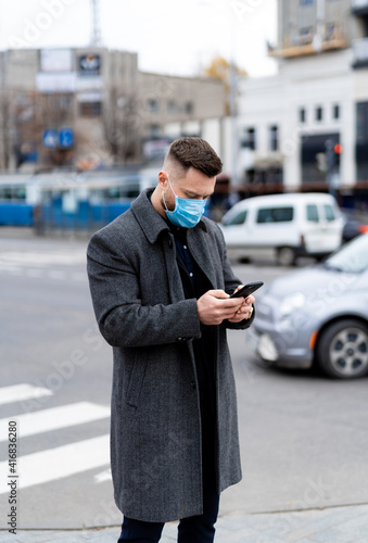 Wallpaper Mural Male in mask types message outdoors. Man in suit, coat and protective mask stands in the city center. Torontodigital.ca