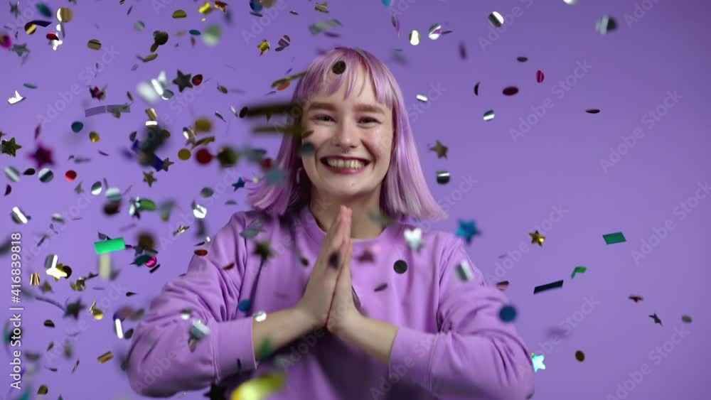 Excited unique woman clapping hands, having fun, screaming WOW, rejoices over confetti rain in studio. Extraordinary girl with violet dyed hairstyle. Concept of celebrating, party, winning Excited unique woman clapping hands, having fun, screaming WOW, rejoices over confetti rain in studio. Extraordinary girl with violet dyed hairstyle. Concept of celebrating, party, winning