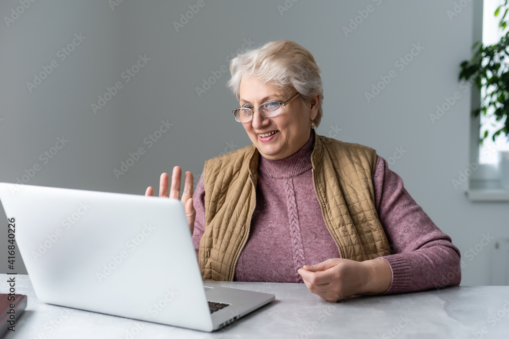 Elderly woman making video call on laptop, waving at screen, chatting with children, free space Elderly woman making video call on laptop, waving at screen, chatting with children, free space