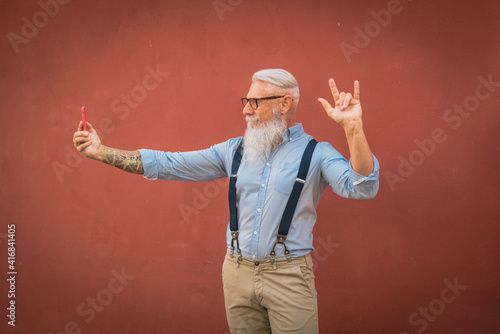 an older man in hipster clothes and glasses and a long white beard walks around talking on the phone focus on head