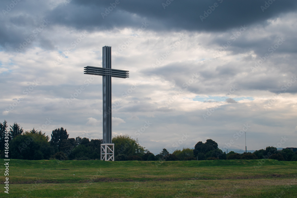 Huge cross in a park with some green trees, on a cloudy day and some hills in the background Huge cross in a park with some green trees, on a cloudy day and some hills in the background