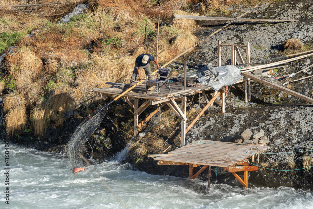A Native American man catching a salmonwith a large dip net from a fishing  platform at the Shearers Bridge rapids onthe Deschutes River near Tygh  Valley, Oregon Stock Photo